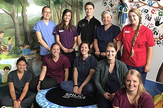 Photo of ten physical therapy students posing together in front of a painted mural in an Ecuadorian childcare facility. 